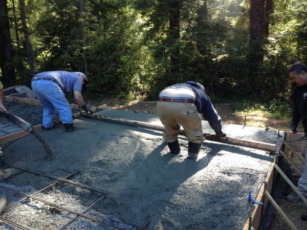 A wood post is dragged along the top layer to flatten the concrete